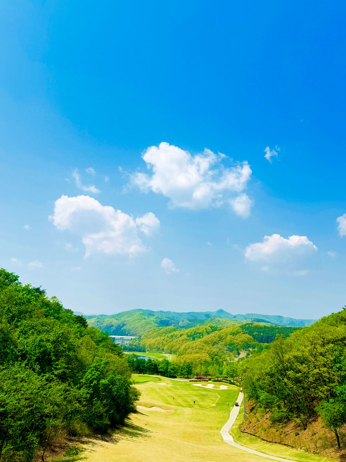A fairway stretching through green hills below scattered clouds. Illustrative photograph; not the reported event or venue.